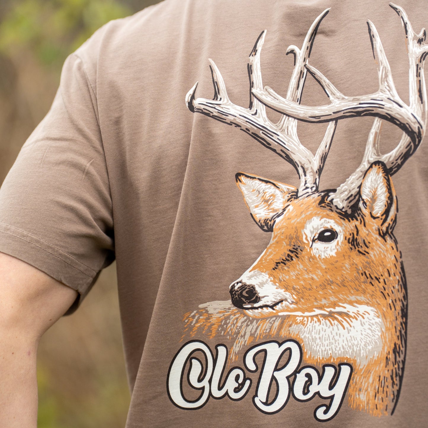 Brown t-shirt with a deer graphic and 'Ole Boy' text on the back, worn by a person.