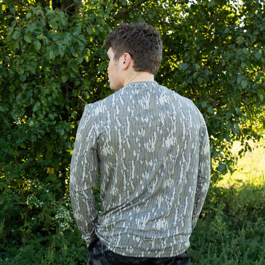 Person wearing a patterned shirt and black shorts standing in a green outdoor setting