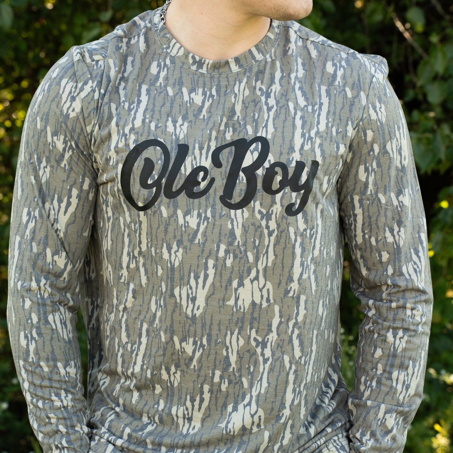 Person wearing a camouflage long-sleeve shirt with 'Ole Boy' text in an outdoor setting