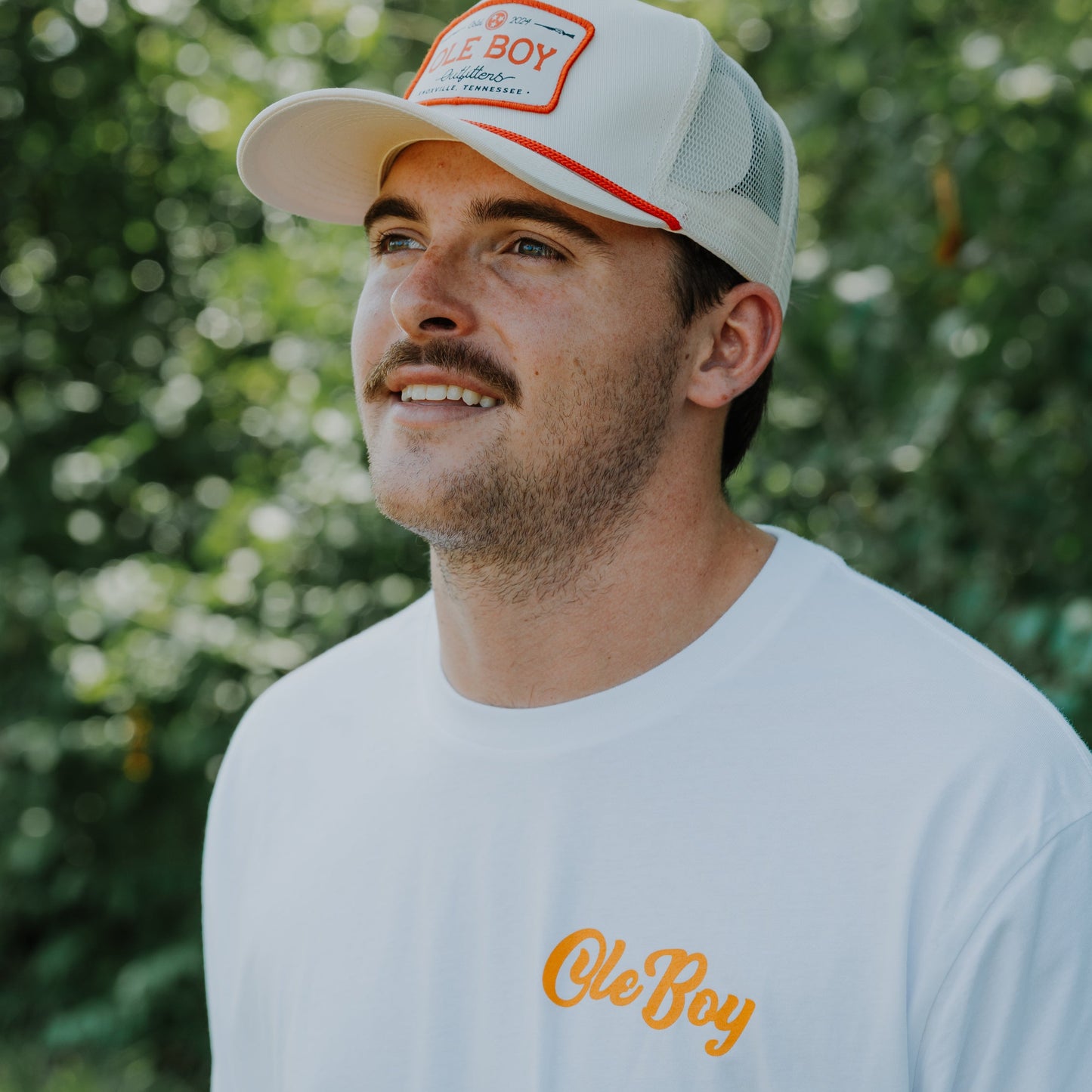 Man wearing a cap and t-shirt with 'Ole Boy' branding outdoors
