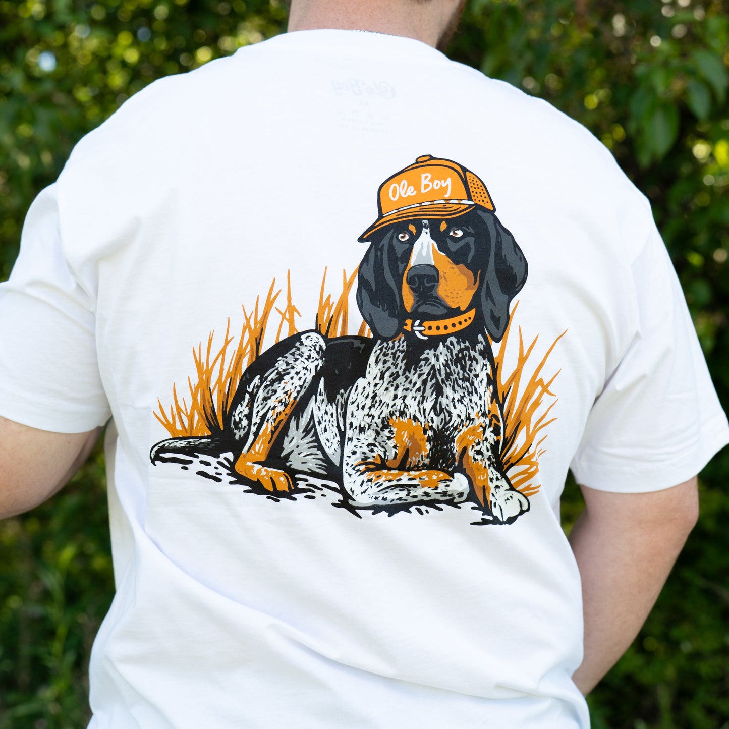 Person wearing a white t-shirt with a graphic of a dog and 'Ole Boy' cap on the back, standing outdoors.