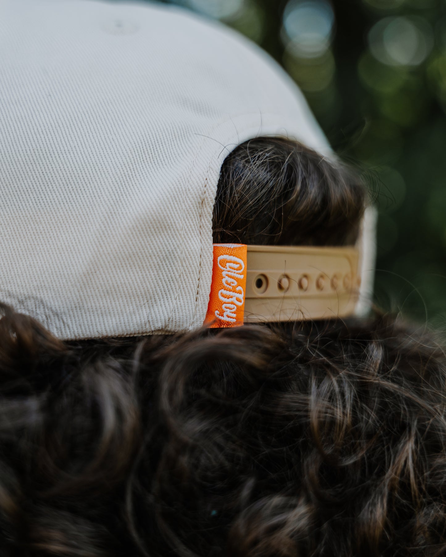 Dog wearing a cap with a visible brand tag against a blurred natural background