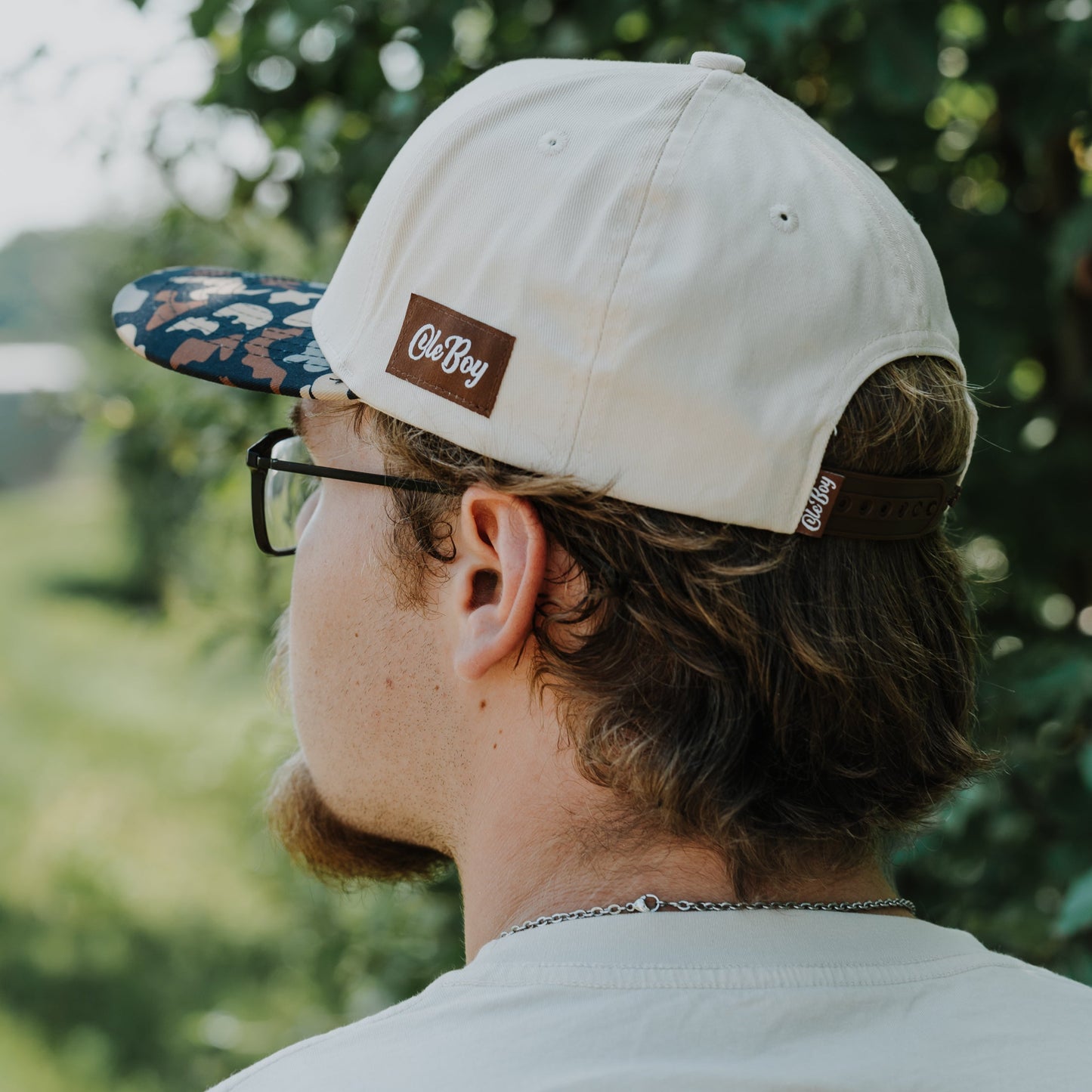 Person wearing a beige cap with an ole boy logo, looking away from the camera in a natural setting.