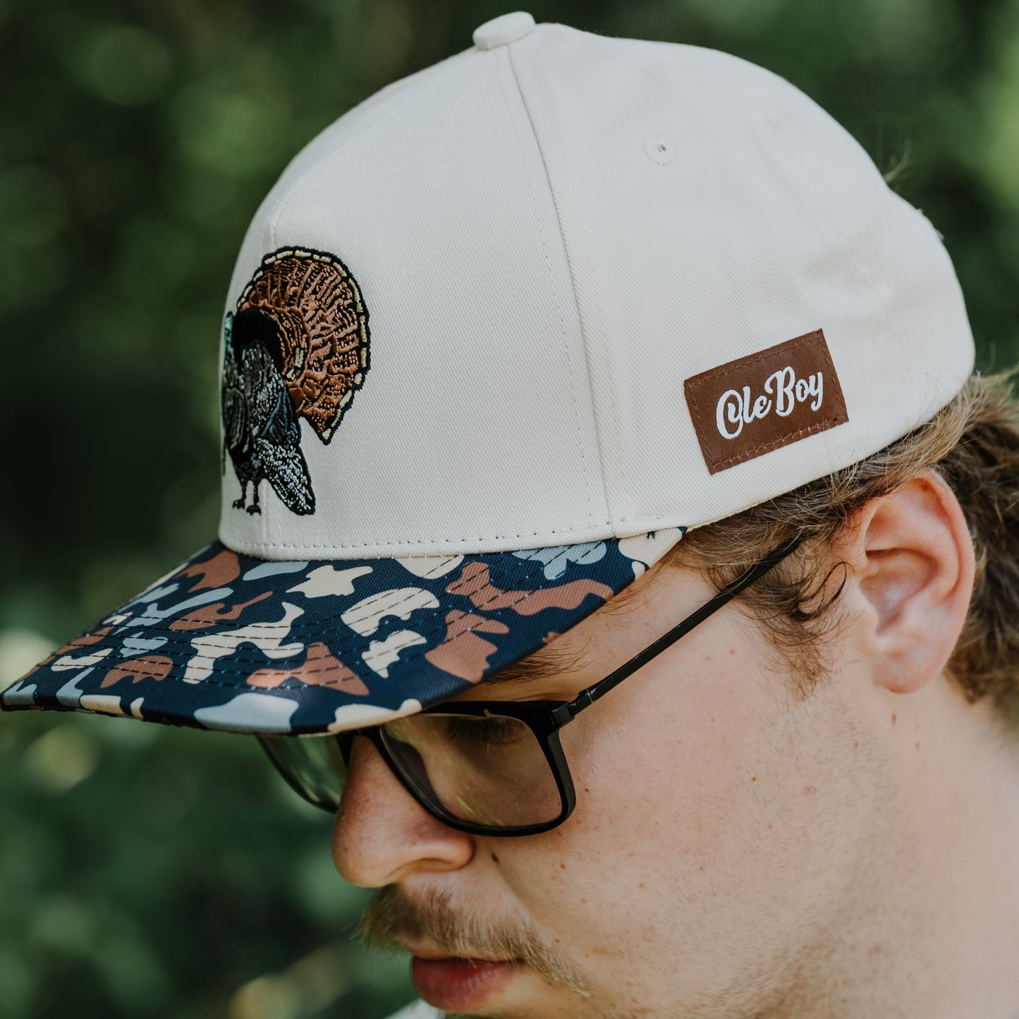 Man wearing a cap with a turkey design and 'Ole Boy' logo, outdoors.