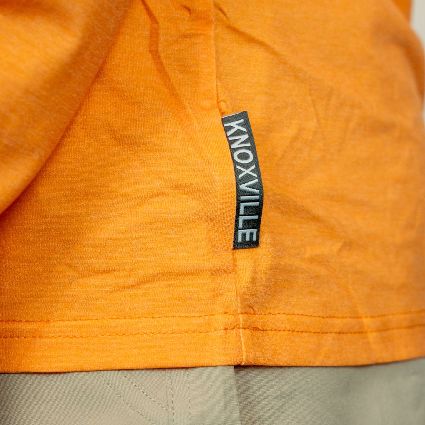 Close-up of an orange garment with a 'Knoxville' label on a neutral background