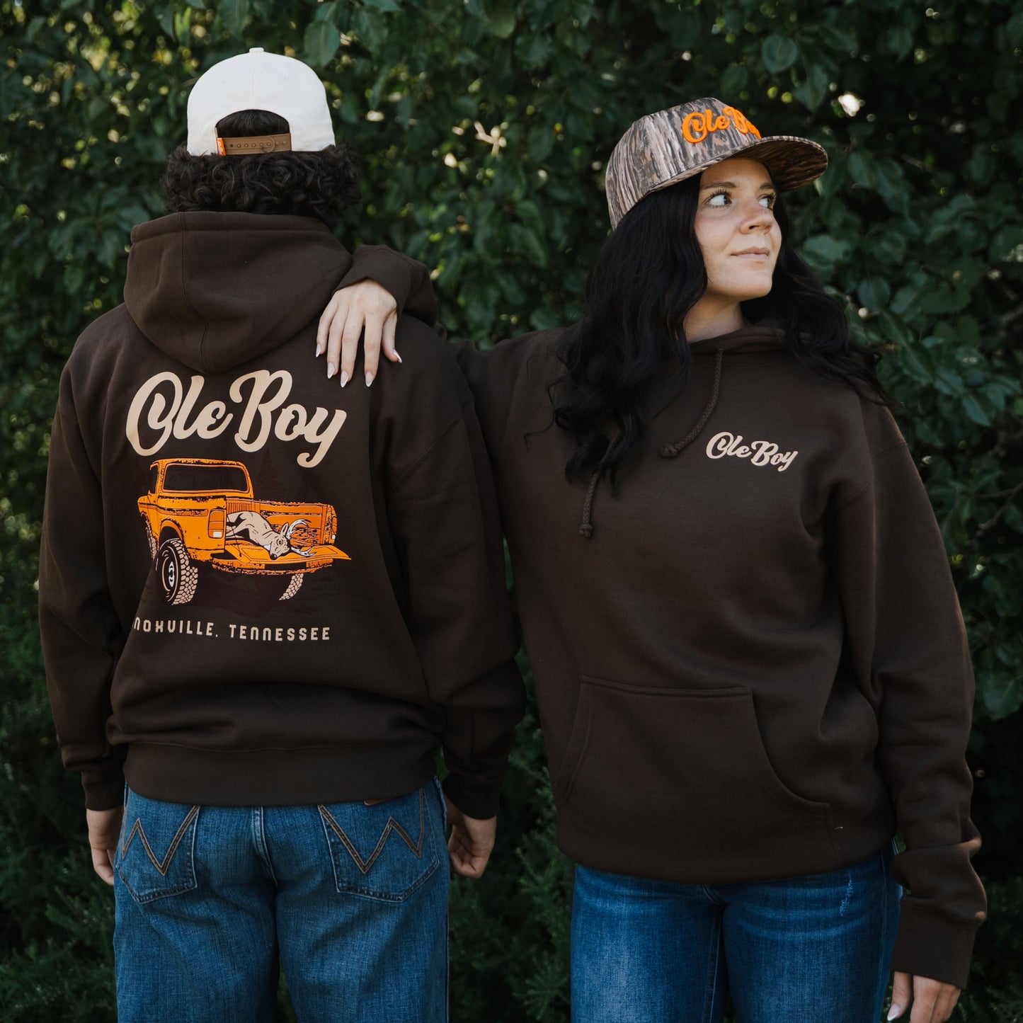 Two people wearing brown hoodies with 'Ole Boy' branding, one with a graphic of an orange truck on the back.