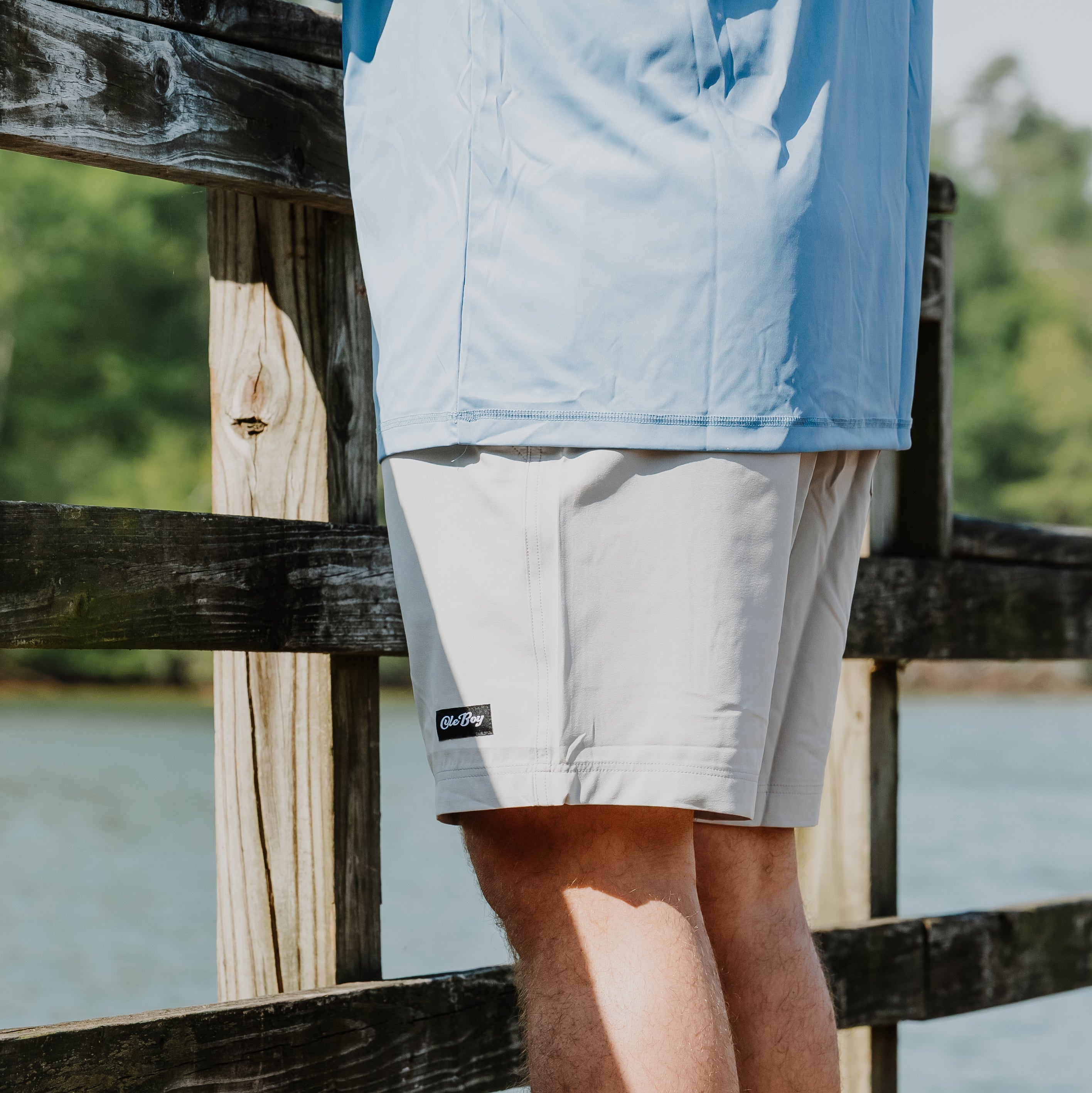 Person wearing light blue shirt and gray ole boy shorts standing on a wooden bridge over water.