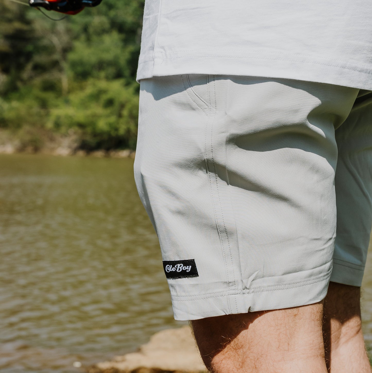 Person wearing light-colored shorts with a ole boy brand logo near a body of water.