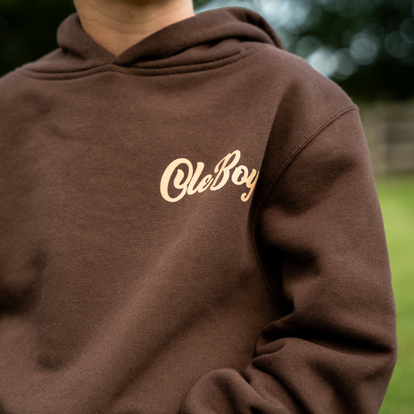 Brown hoodie with 'Ole Boy' text on a blurred outdoor background