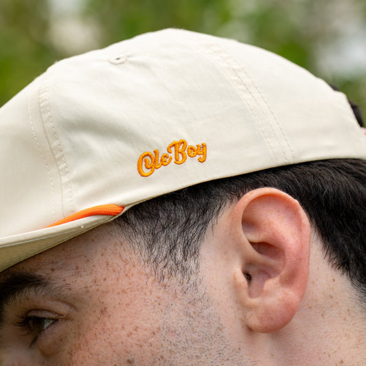 Beige cap with 'Ole Boy' logo worn by a person, blurred green background