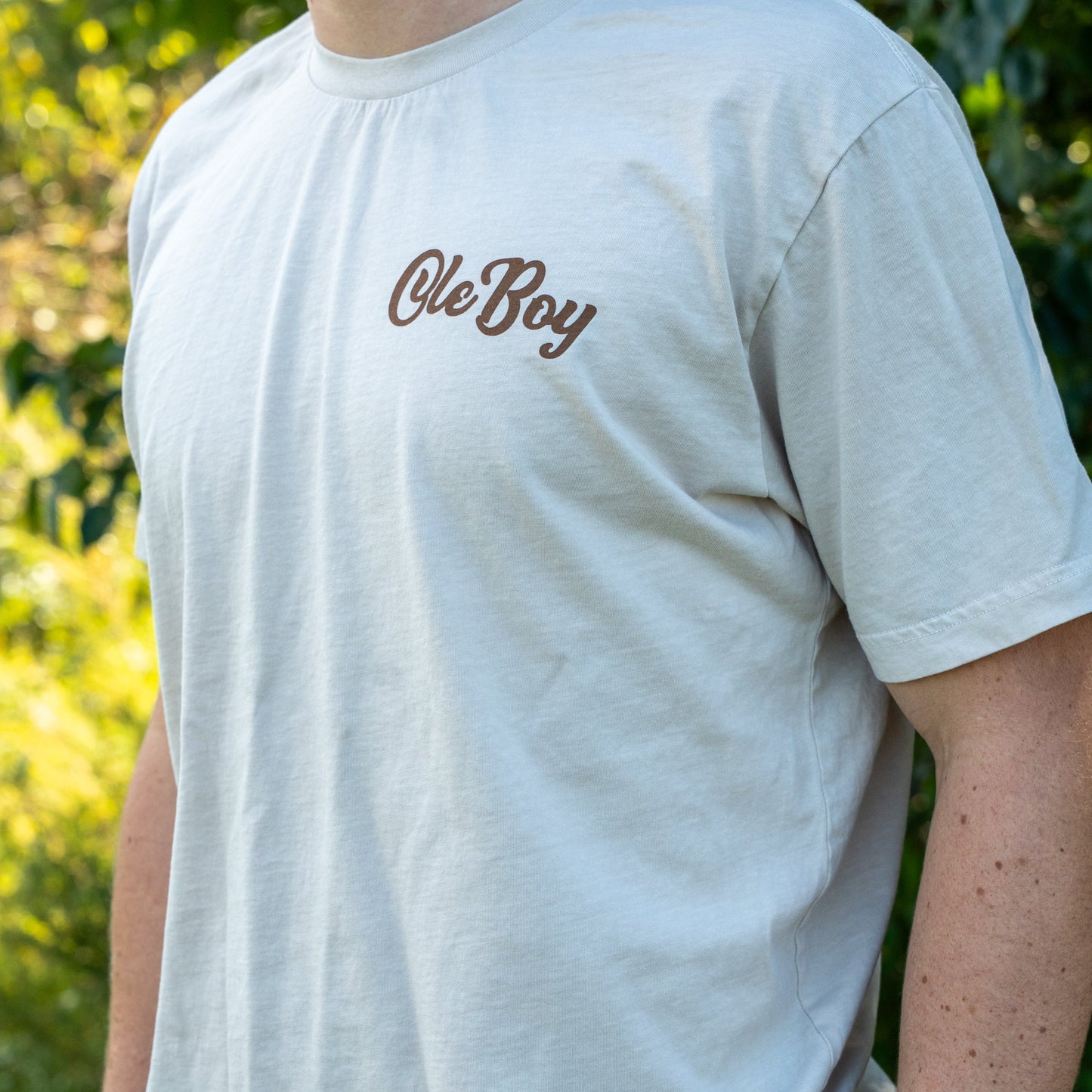 Person wearing a light gray t-shirt with 'Ole Boy' text, standing outdoors.