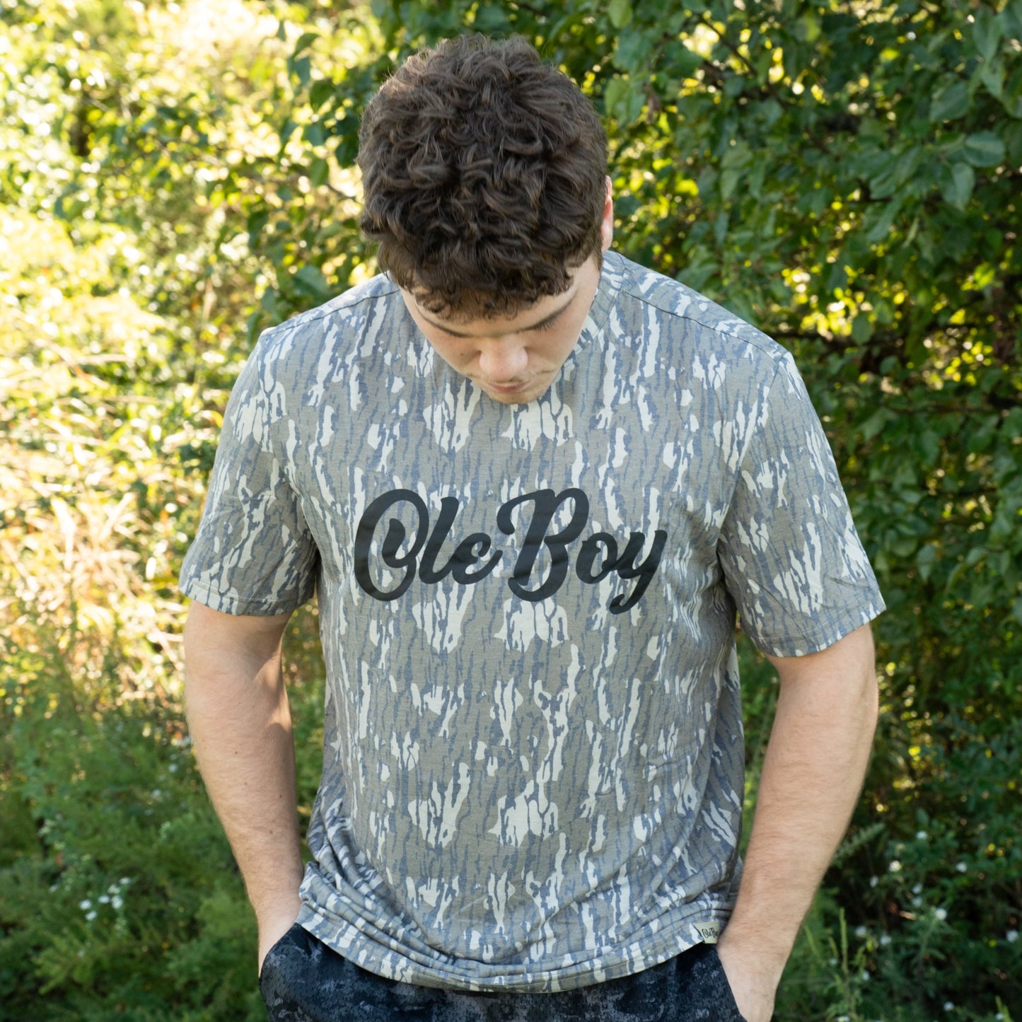 Person wearing a camo 'Ole Boy' t-shirt outdoors with greenery in the background