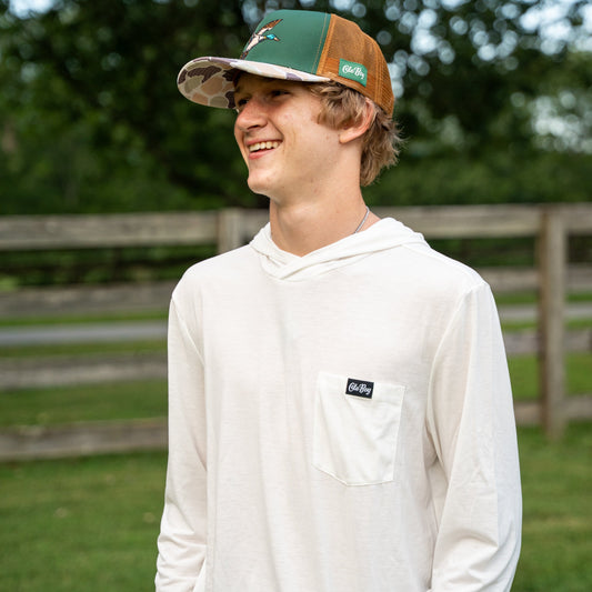 Person wearing a white hoodie with a logo and a cap in an outdoor setting