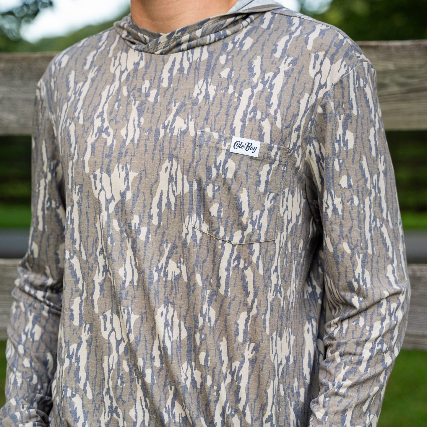 Person wearing a camouflage long-sleeve shirt with a brand logo, standing outdoors.