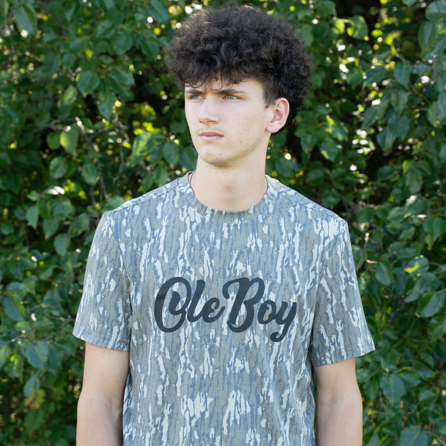 Person wearing a camouflage t-shirt with 'Ole Boy' text in front of green foliage