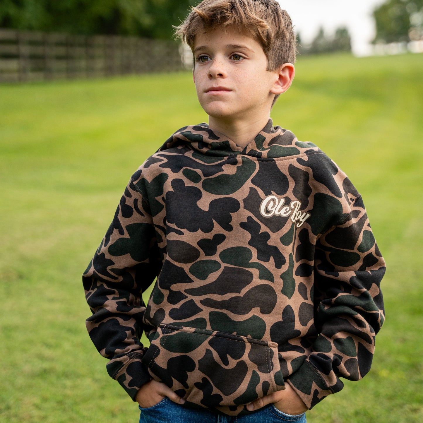 Child wearing a camouflage hoodie with 'Ole-Boy' logo outdoors on grass