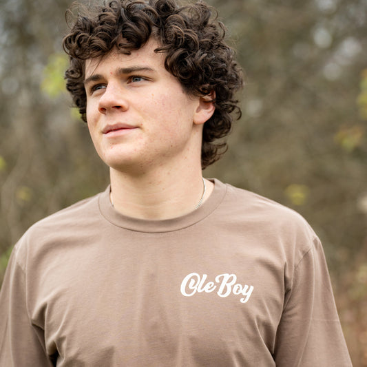 Person wearing a brown t-shirt with 'Ole Boy' text outdoors
