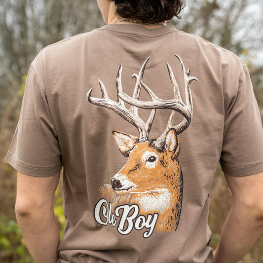 Person wearing a brown t-shirt with a deer graphic and 'Ole Boy' text in an outdoor setting