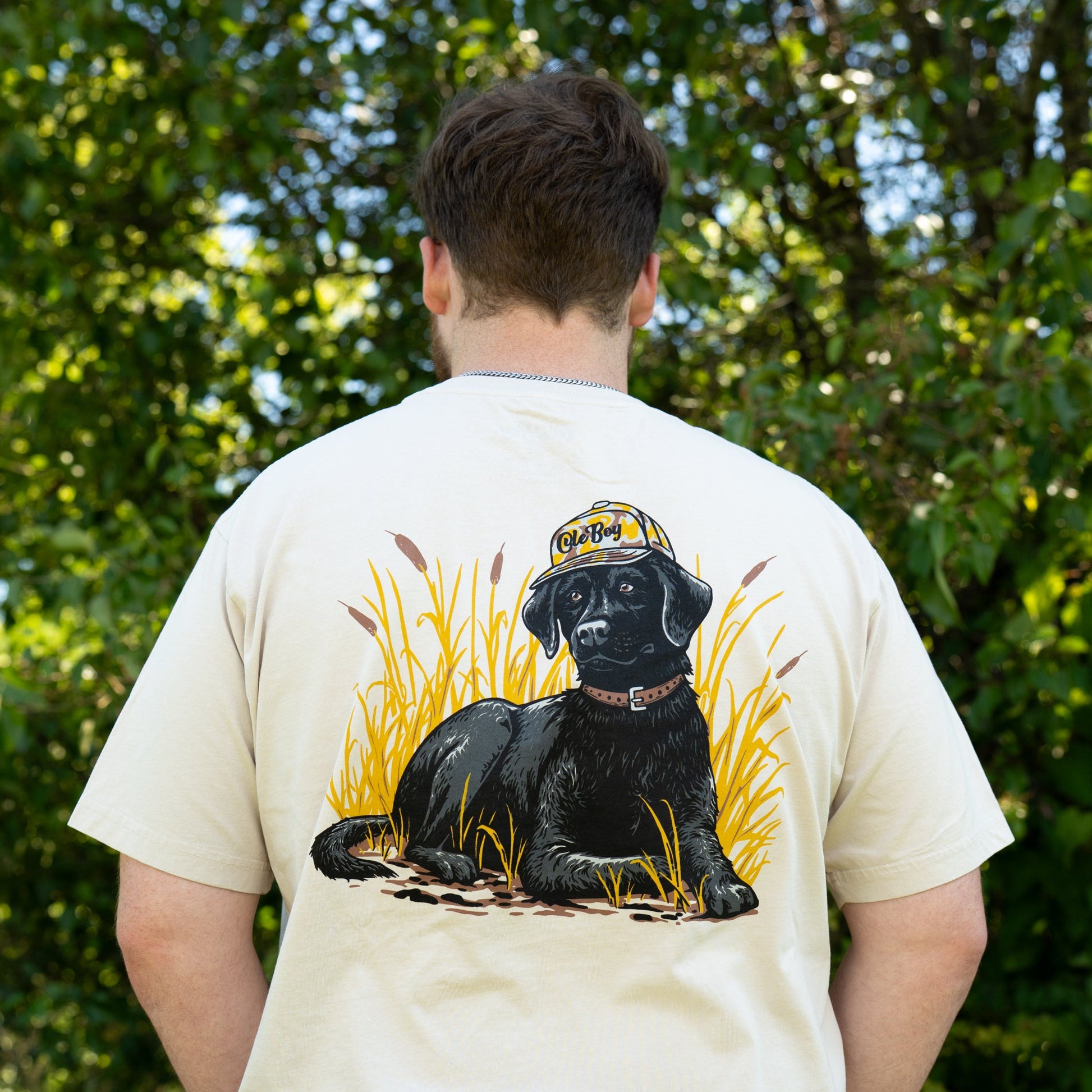 Person wearing a beige t-shirt with a black dog graphic in a natural setting