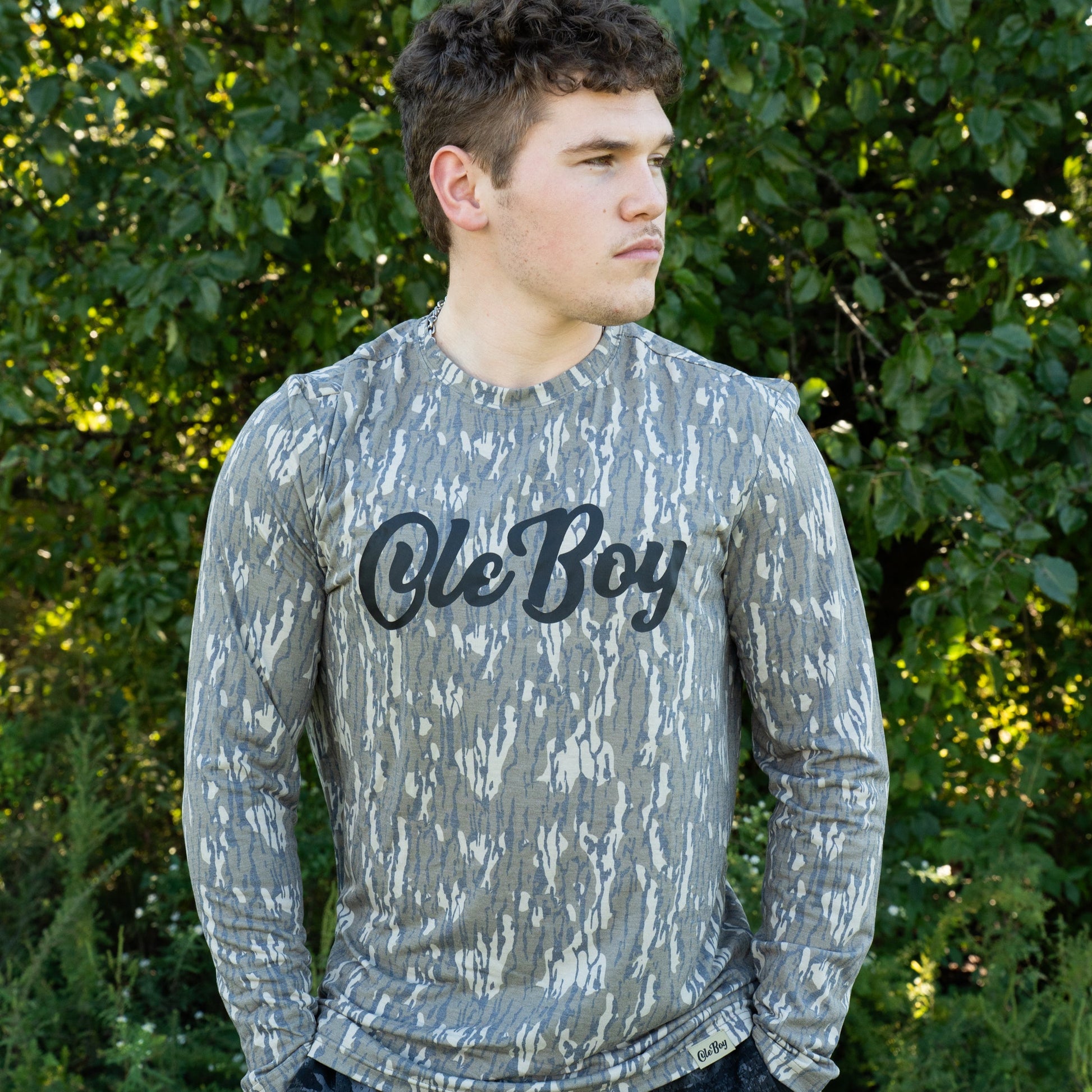 Person wearing a camouflage long-sleeve shirt with 'Ole Boy' text outdoors.
