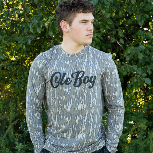Person wearing a camouflage long-sleeve shirt with 'Ole Boy' text outdoors.