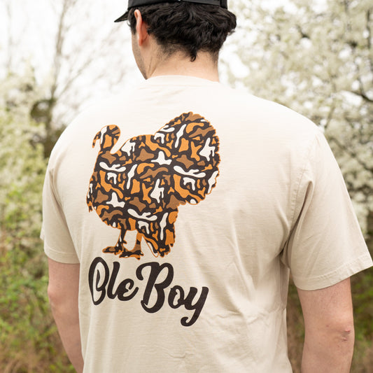Person wearing a beige t-shirt with a graphic design and text 'Ole Boy' outdoors.