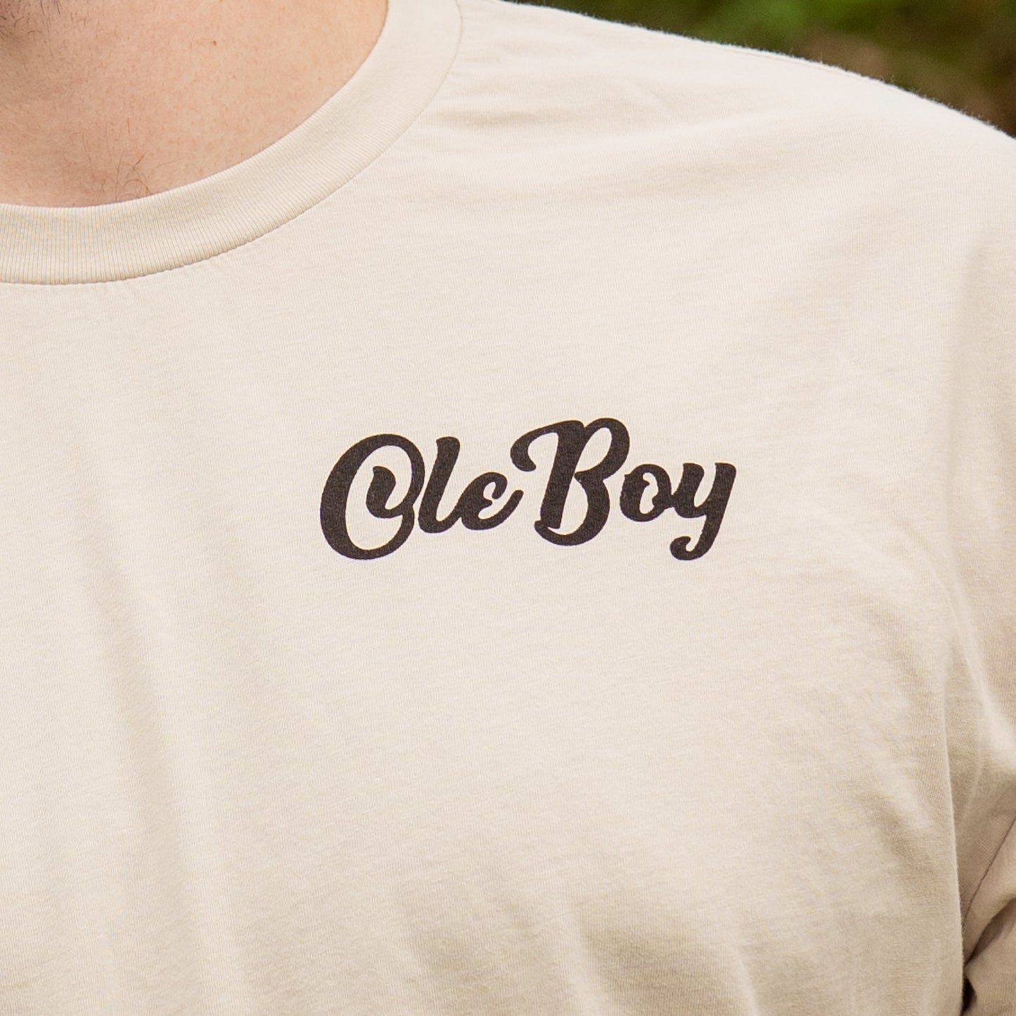 Beige t-shirt with 'Ole Boy' text on a person wearing it, with a blurred natural background.