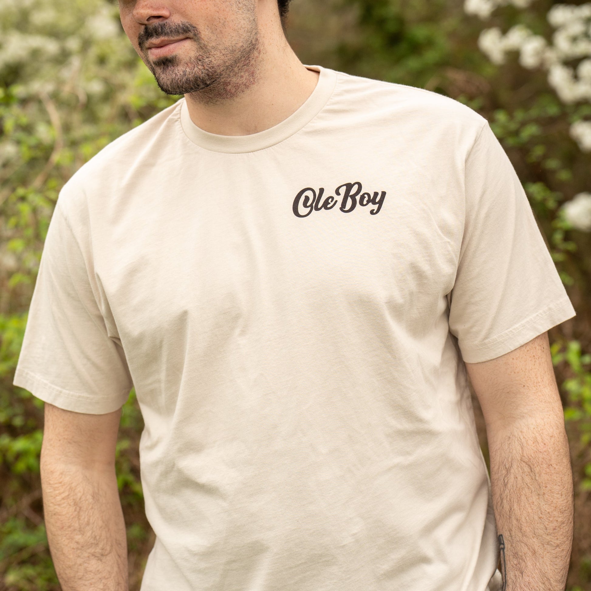 Man wearing a beige t-shirt with 'Ole Boy' text in a forest setting