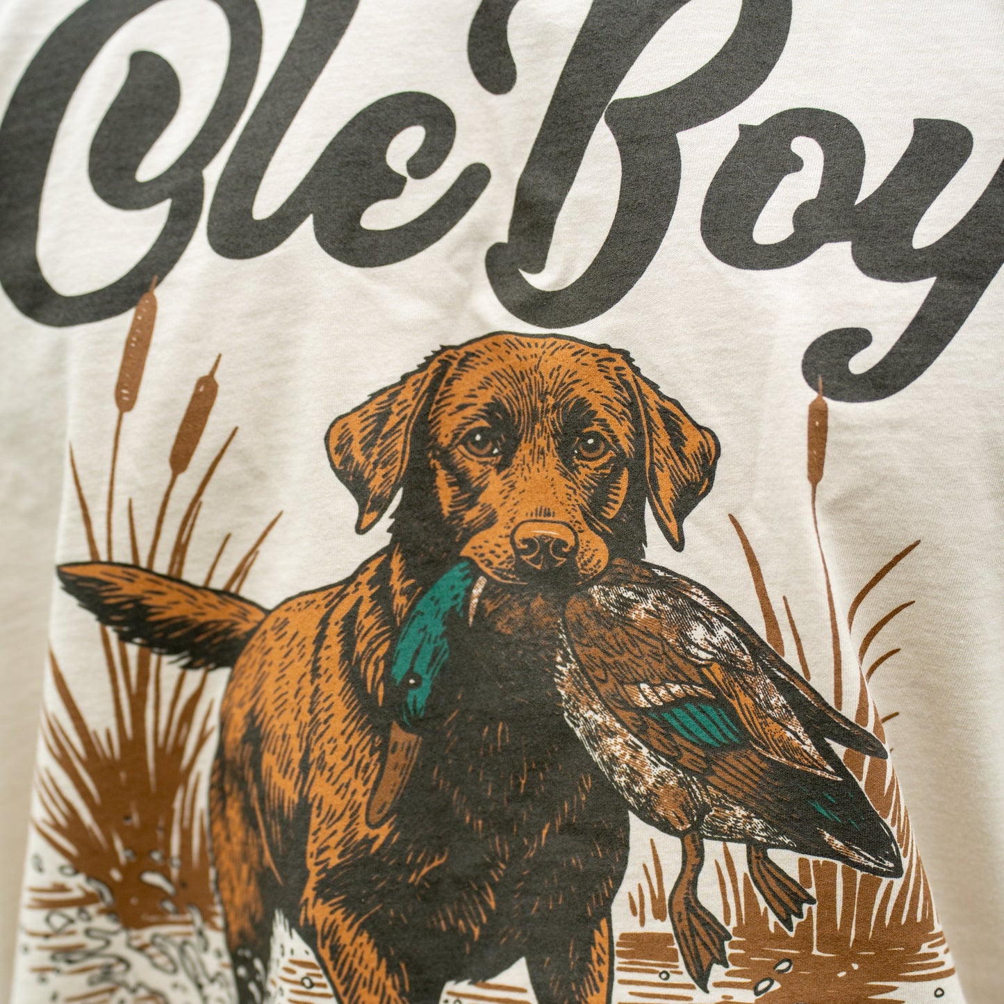 T-shirt with a graphic of a dog holding a duck and the text 'Ole Boy' on a beige background.