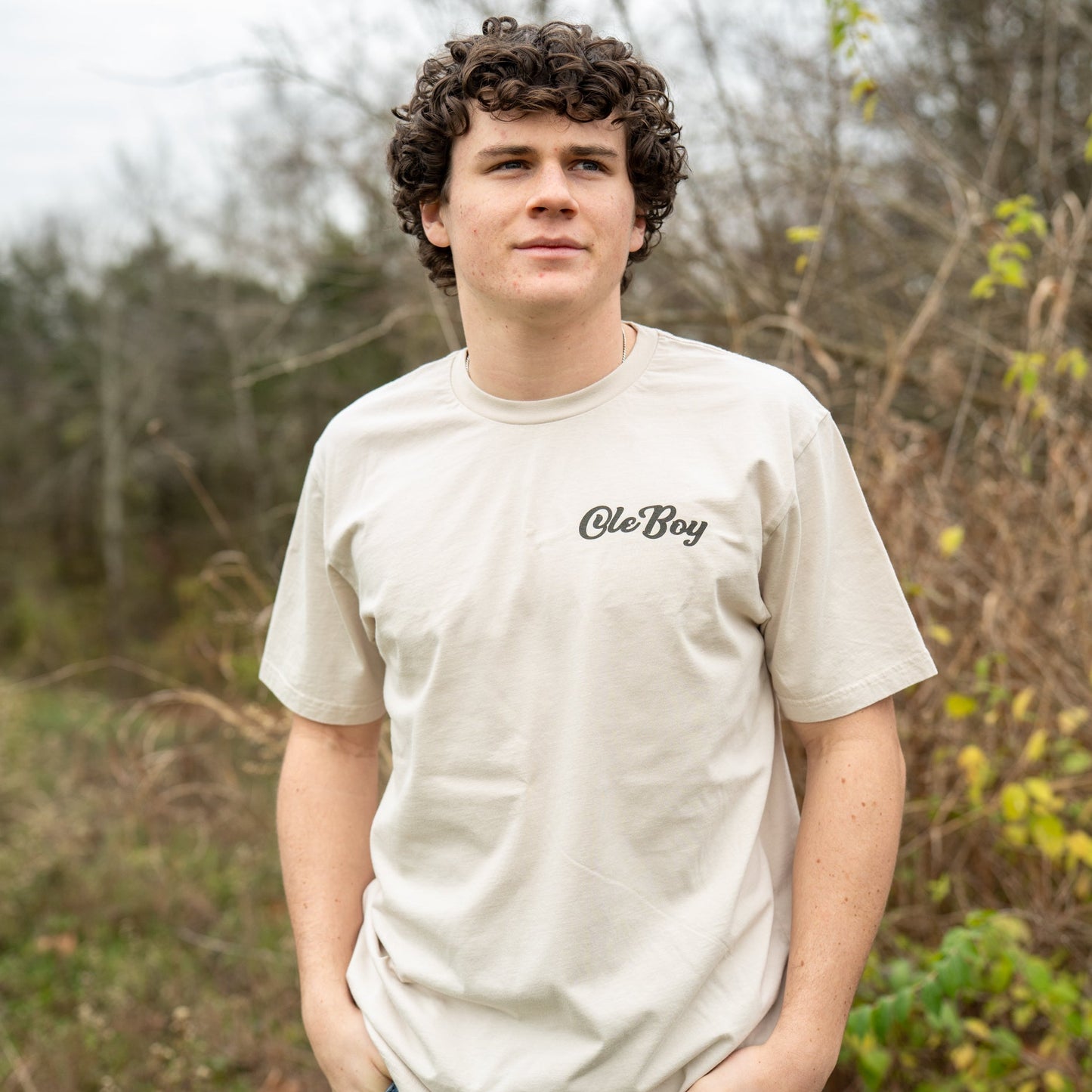 Person wearing a 'Ole Boy' t-shirt standing outdoors with trees in the background