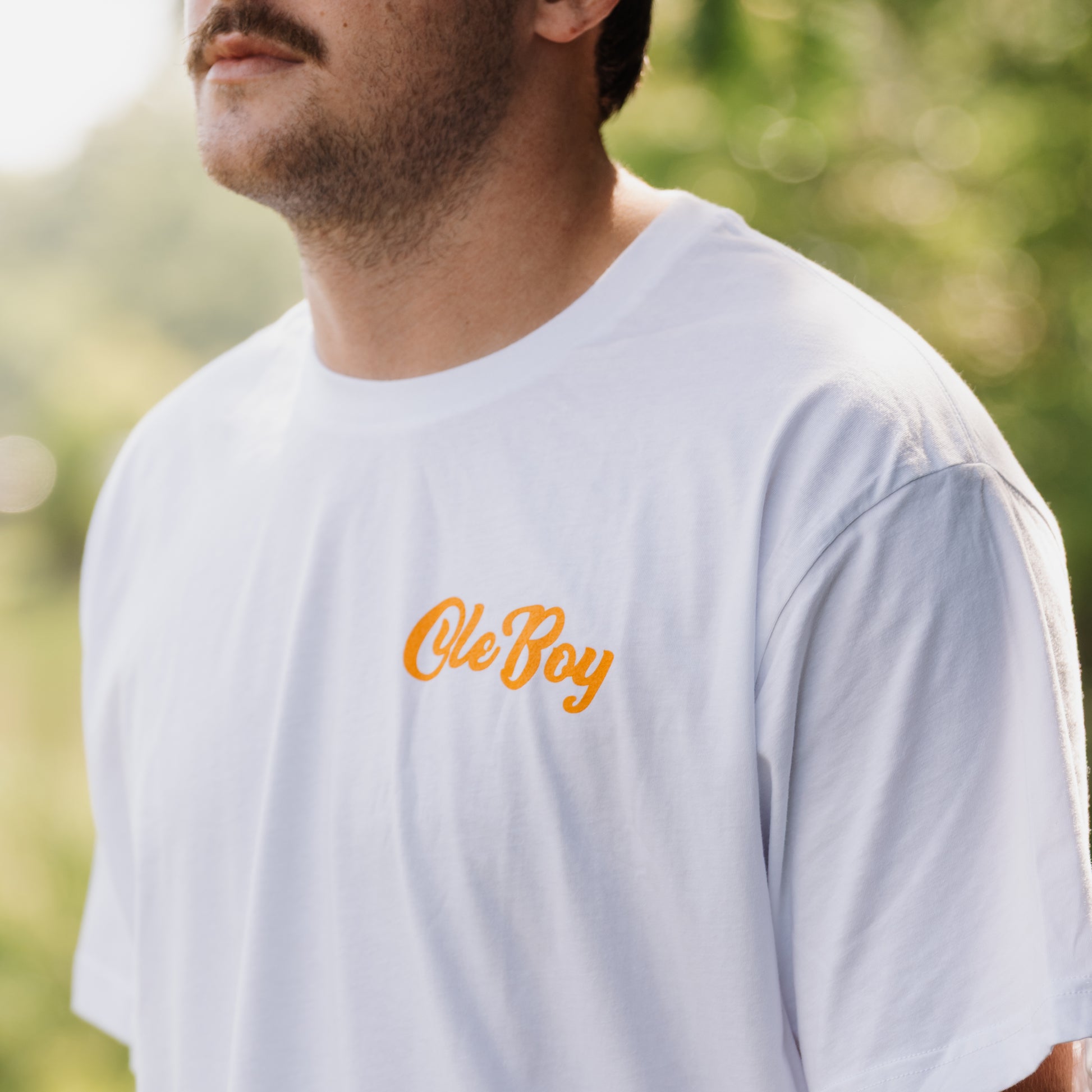 Man wearing a white t-shirt with 'Ole Boy' text in orange outdoors.