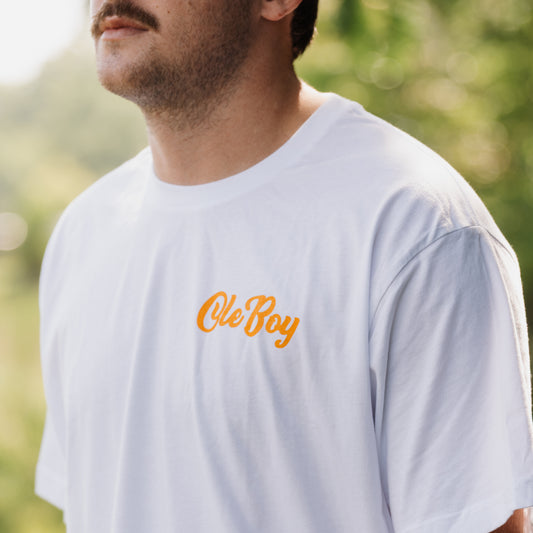 Man wearing a white t-shirt with 'Ole Boy' text in orange outdoors.
