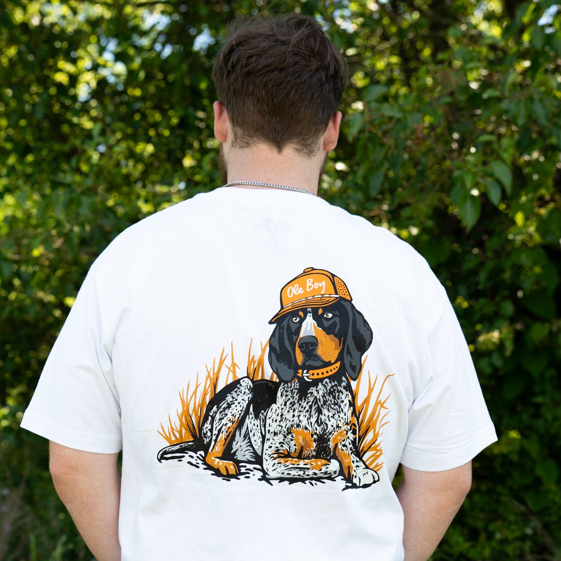 Person wearing a white t-shirt with a coonhound dog graphic on the back, standing in a natural setting.