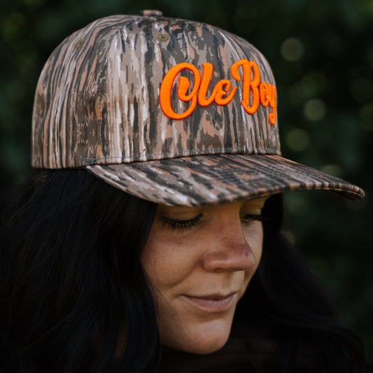 Person wearing a camouflage cap with 'Ole Boy' text against a blurred green background