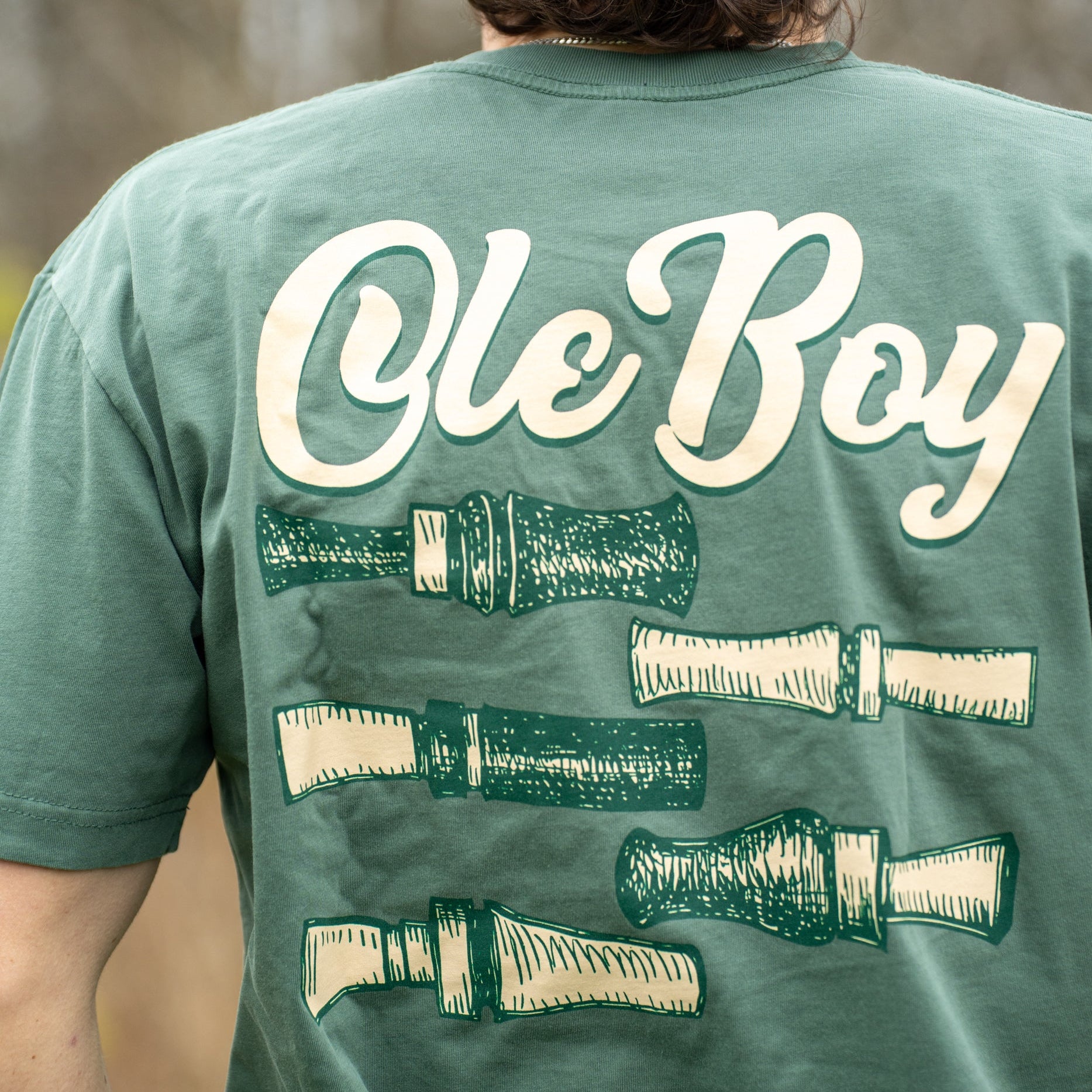 Person wearing a green t-shirt with 'Ole Boy' and duck call designs on the back.