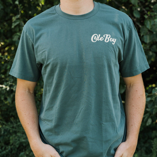 Person wearing a green t-shirt with 'Ole Boy' text against a blurred natural background
