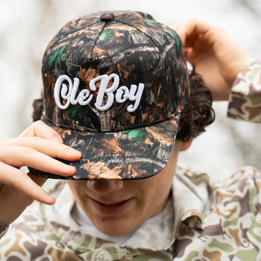 Person wearing a camouflage cap with 'Ole Boy' text, standing against a blurred natural background.