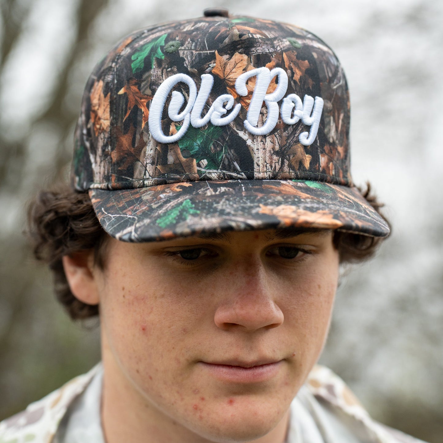 Person wearing a camouflage cap with 'Ole Boy' text against a blurred natural background