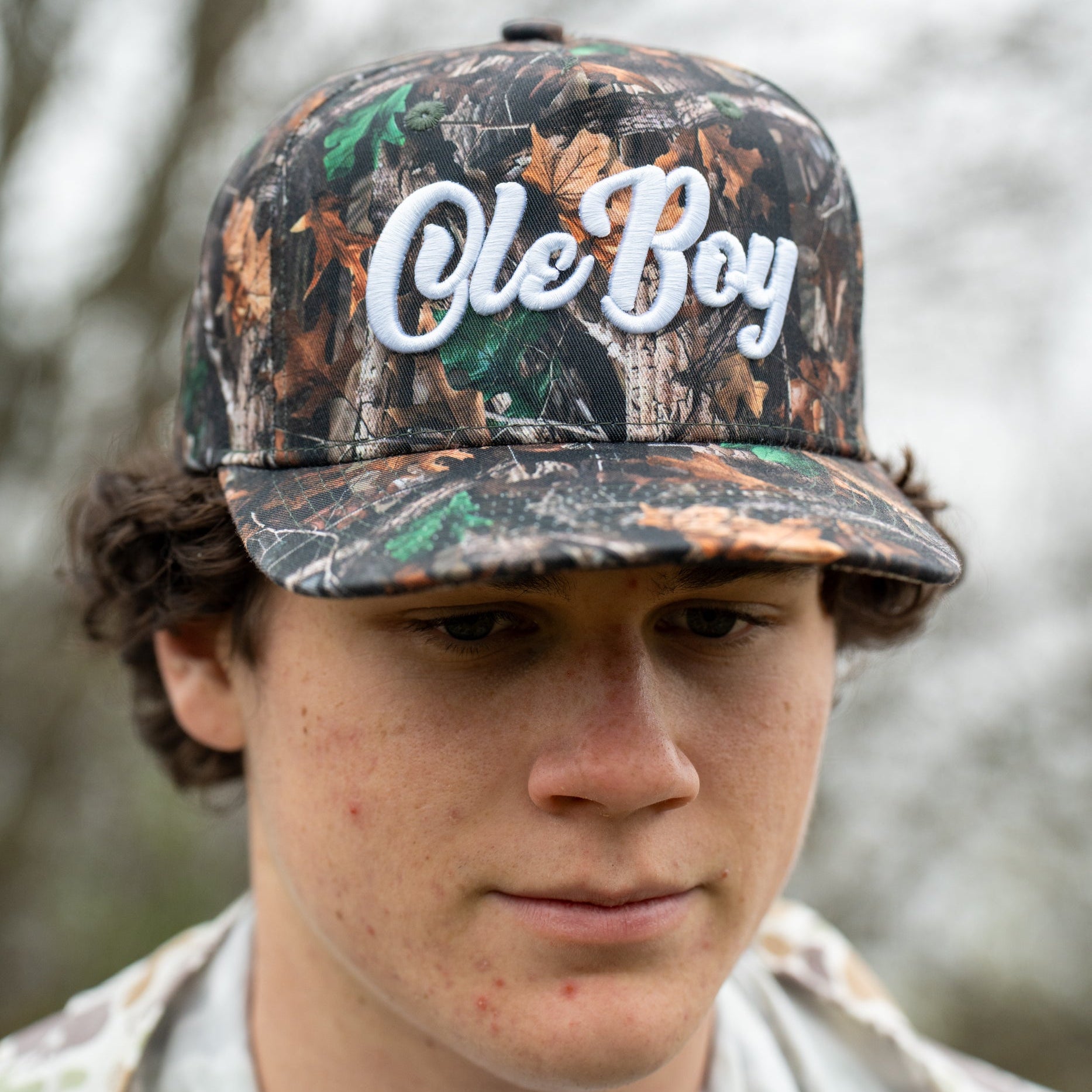 Person wearing a camouflage cap with 'Ole Boy' text against a blurred natural background