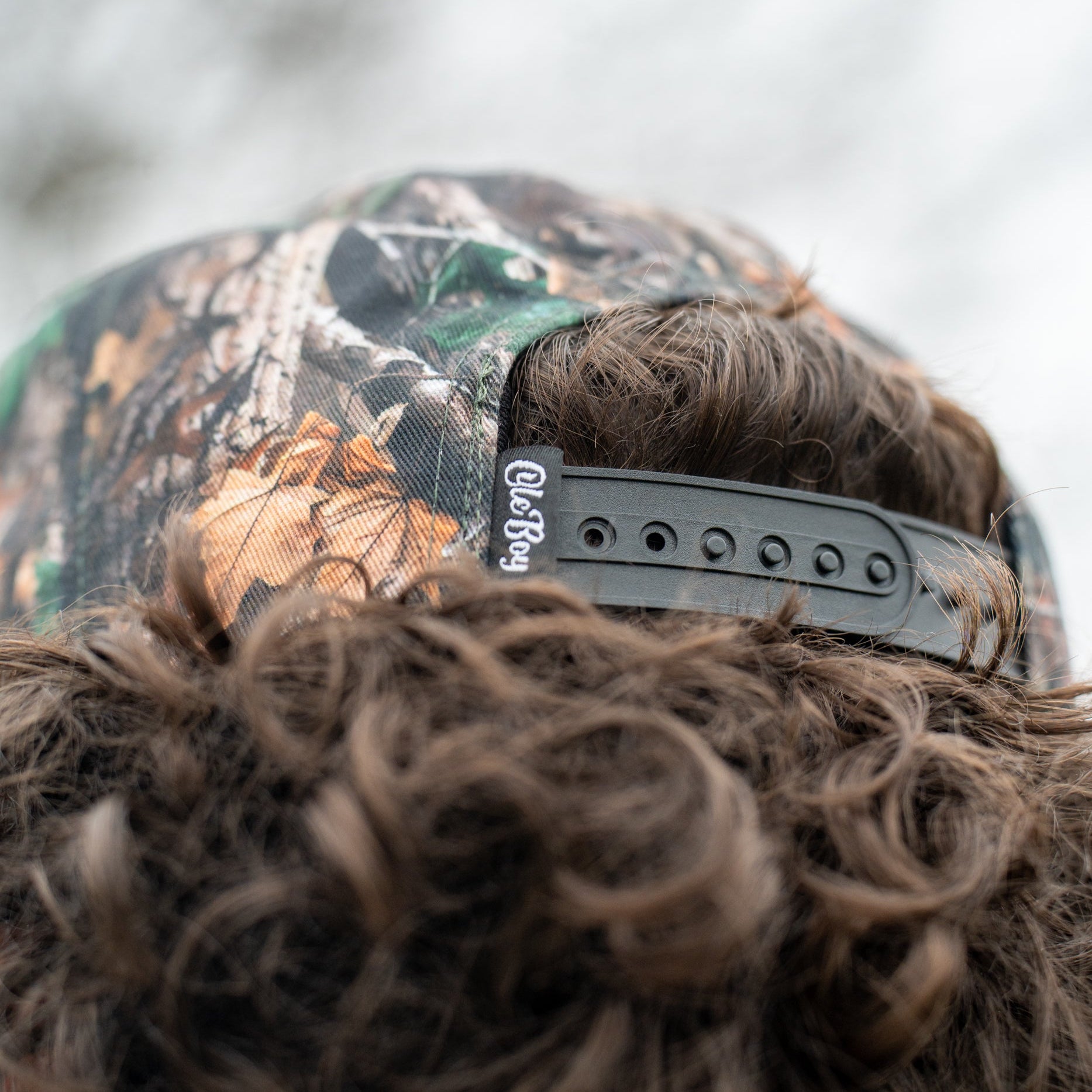 Person wearing a camouflage cap with a brand logo on a blurred natural background