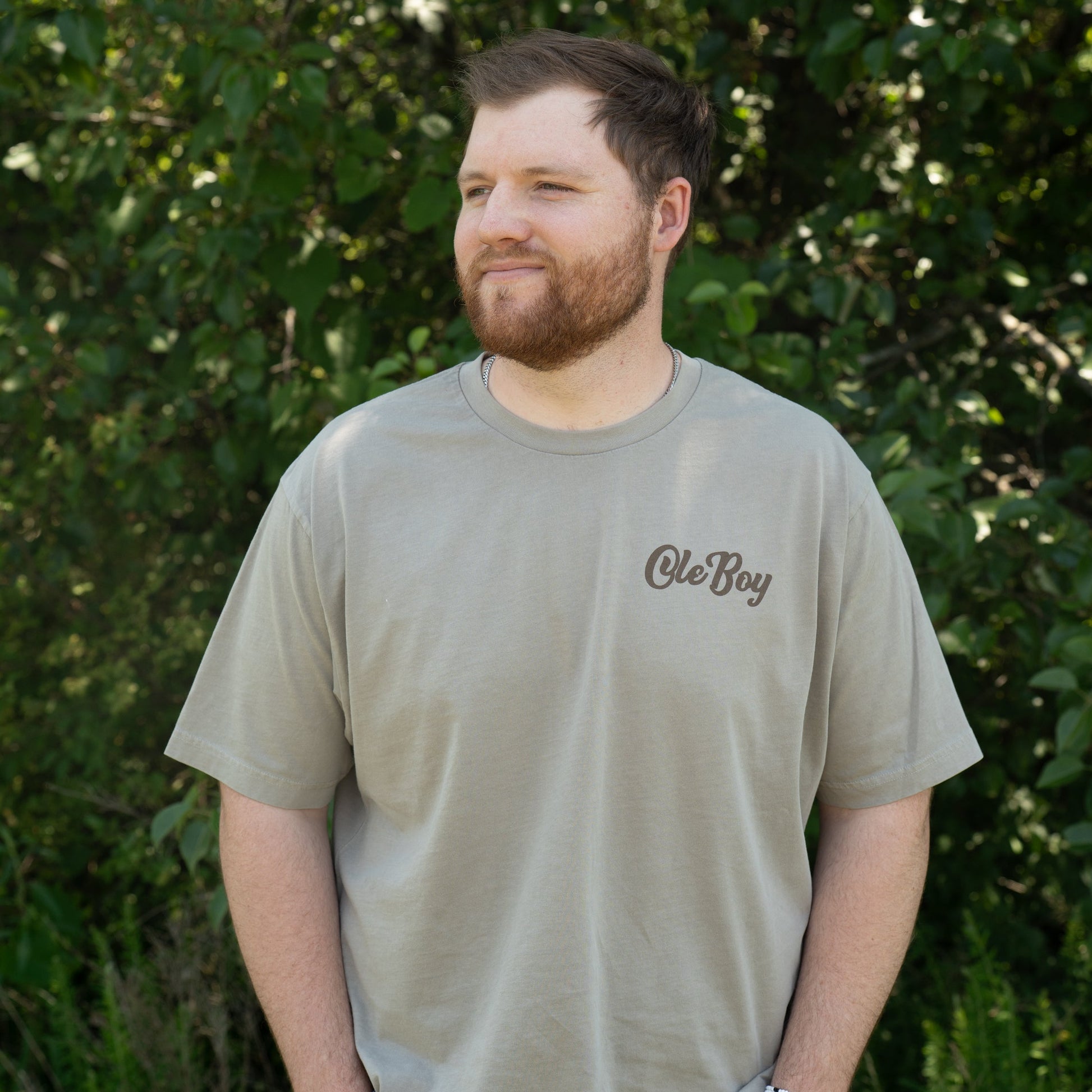 Man wearing a green t-shirt with 'ole Boy' logo standing in front of green foliage