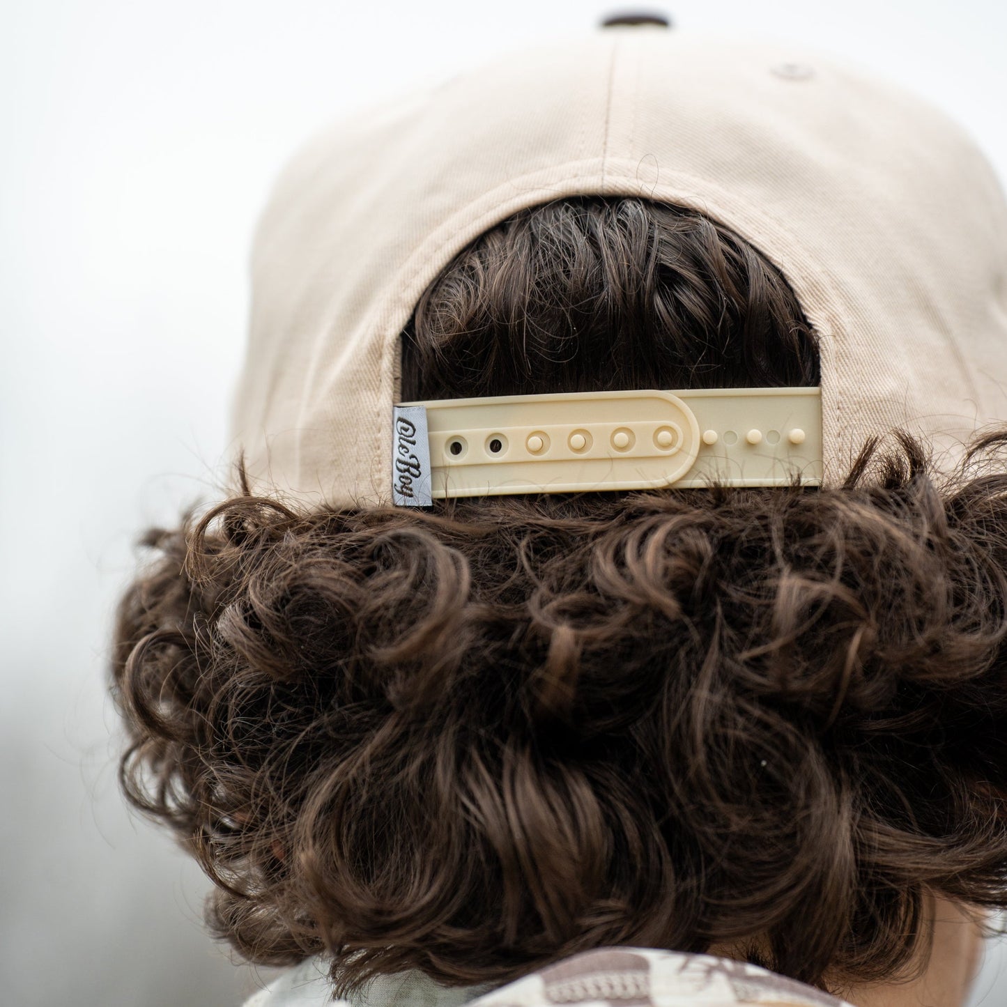 Person wearing a beige cap with a brand logo, facing away from the camera.