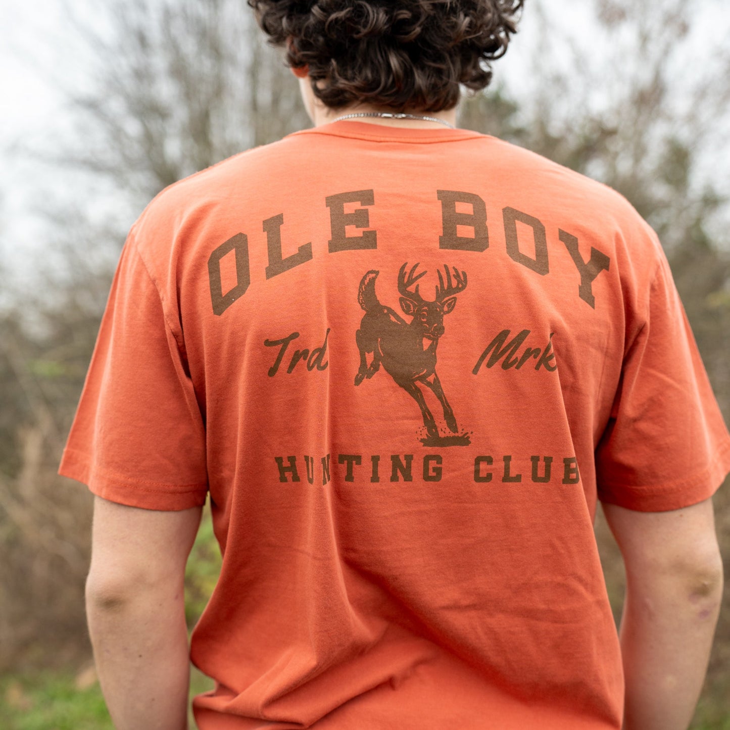 Person wearing an orange t-shirt with 'Ole Boy' and hunting club design outdoors.