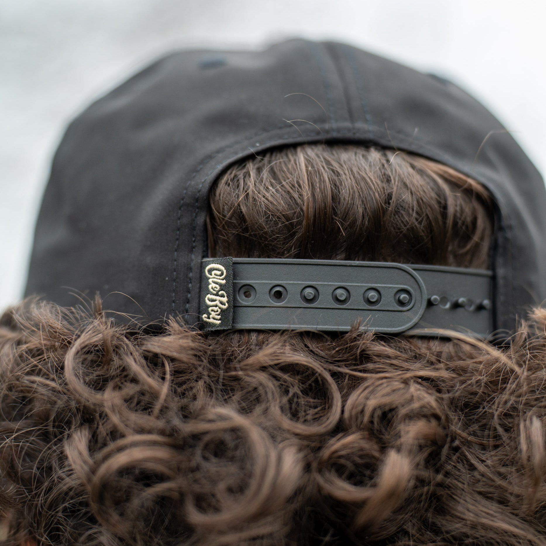 Close-up of a person wearing a black cap with a brand logo, focusing on the cap and hair.