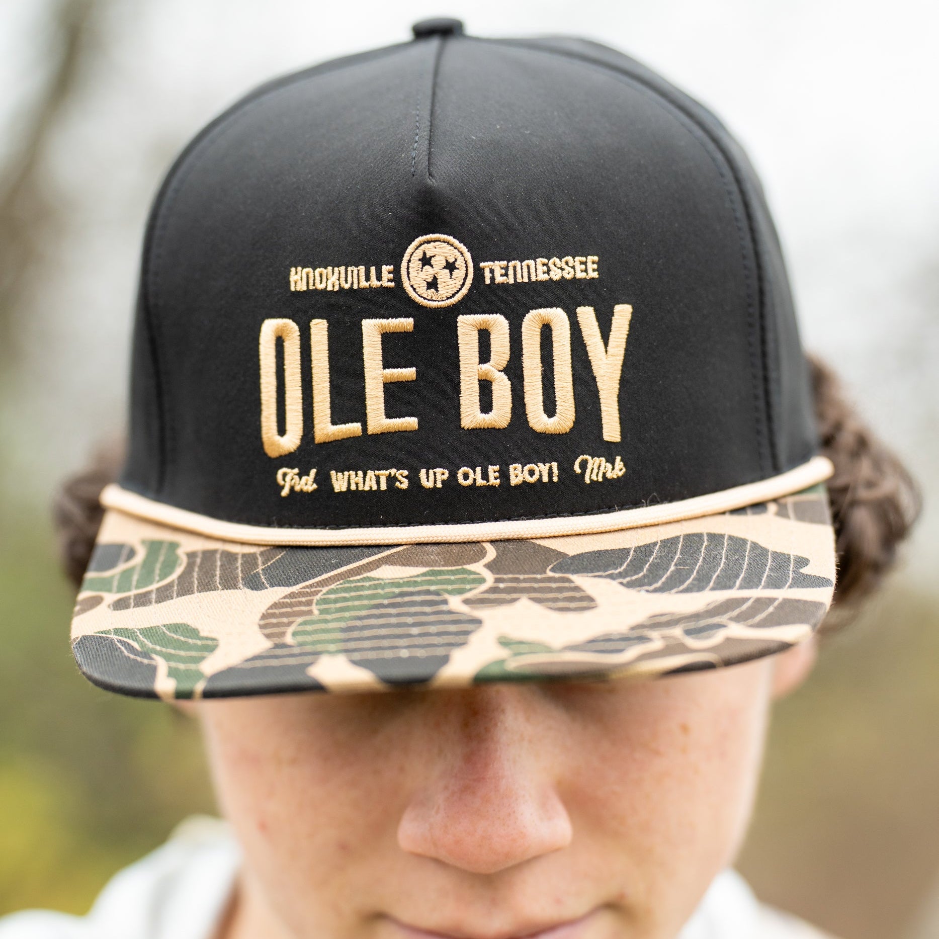 Person wearing a black cap with 'Ole Boy' text and camouflage brim outdoors