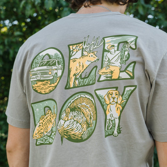 Person wearing a t-shirt with 'OLE BOY' graphic design outdoors.