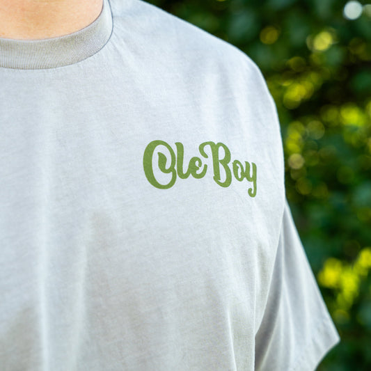Gray t-shirt with 'Ole Boy' text in green on a blurred natural background