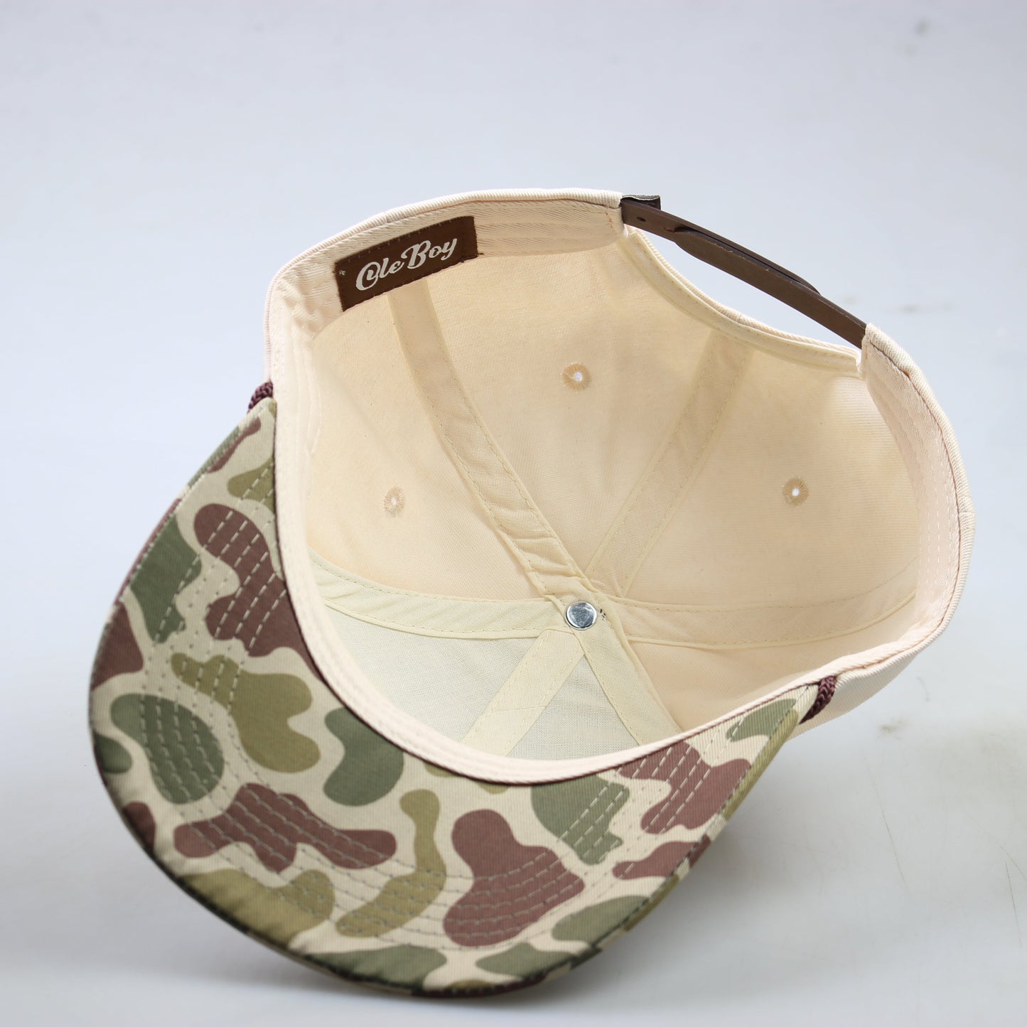 Camouflage-patterned cap with beige interior on a light gray background