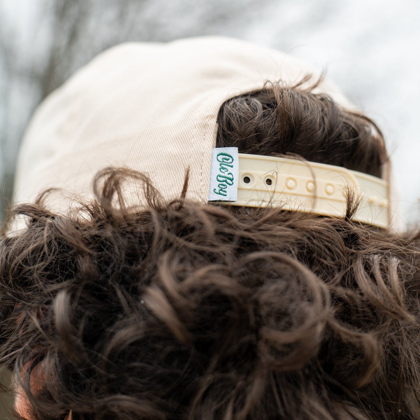 Person wearing a cap with a visible brand logo against a blurred natural background