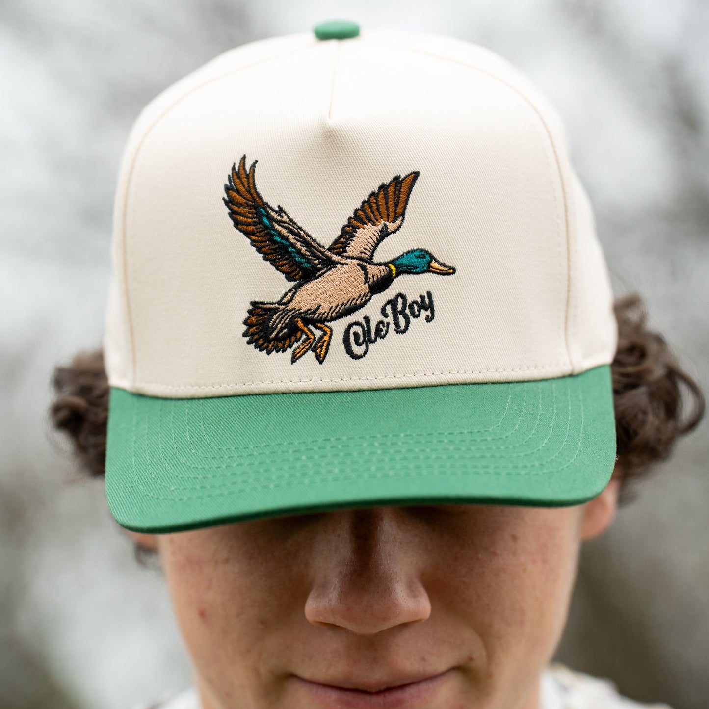 Person wearing a cap with a duck design and 'Ole Boy' text against a blurred natural background